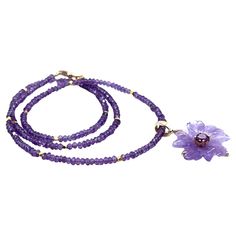 This unique necklace features a beautiful floral amethyst pendant set in 18k yellow gold on a strand of pastel and royal purple amethyst beads. The flower pendant has been hand carved from a single amethyst crystal with delicate purple color, and in the center of the flower sits a sparkling, pinkish purple rhodolite garnet! The strand of deep purple amethyst beads is accented with bright, 18k yellow gold spacers, larger, pastel amethyst beads and is a 14k yellow gold clasp. This is a uniquely ve Luxury Amethyst Pendant Necklace, Luxury Amethyst Gemstone Beads Jewelry, Yellow Gold Flower Necklace With Gemstone, Yellow Gold Flower Shaped Gemstone Necklace, Luxury Yellow Gold Amethyst Necklace, Elegant Amethyst Rondelle Jewelry, Elegant Lavender Necklaces With Gemstone Beads, Elegant Lavender Necklaces With Natural Stones, Luxury Purple Necklace With Gemstone Beads