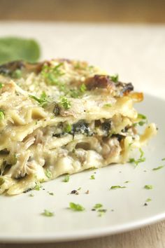 a white plate topped with lasagna covered in cheese and toppings next to a green leaf