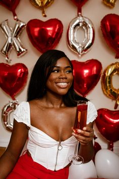 a woman in a red skirt holding a glass of wine with balloons and heart - shaped decorations behind her