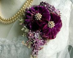 a close up of a purple flower on a white lace corsage with pearls