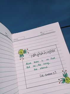 an open book with arabic writing on it and flowers painted on the pages, in front of a blue sky