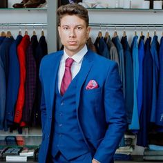 a man in a blue suit and red tie standing next to a rack of shirts