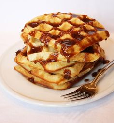 a stack of waffles covered in syrup on a white plate with a fork