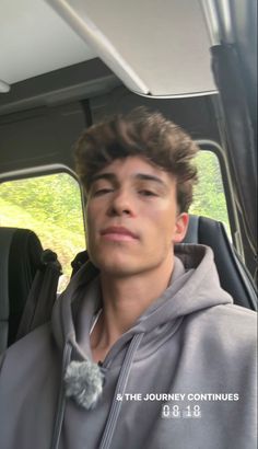 a young man sitting in the back seat of a car wearing a gray hoodie