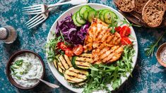 grilled chicken and veggies on a white plate with cucumbers, tomatoes, lettuce