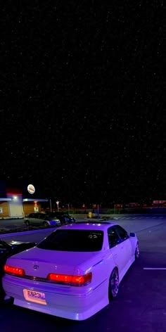 a purple car parked in a parking lot at night with the lights on and stars above