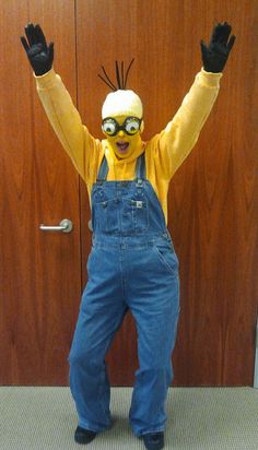 a man dressed as a minion with his hands in the air and wearing overalls