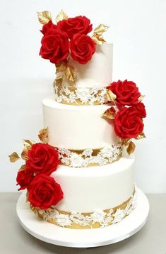 a three tiered wedding cake with red roses on top and gold leaves around the edges