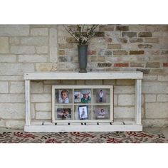 a white shelf with pictures and flowers on it in front of a brick wall,