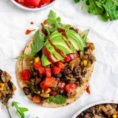 an overhead view of a tortilla topped with black beans, avocado and tomatoes