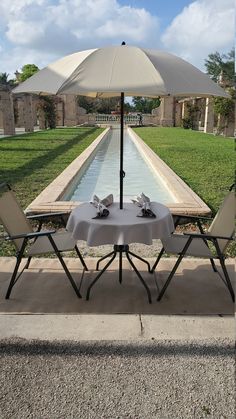 two chairs and an umbrella sitting on the side of a road next to a pool