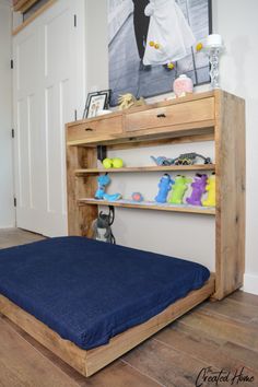 a bed with a blue blanket on top of it next to a wooden shelf filled with stuffed animals