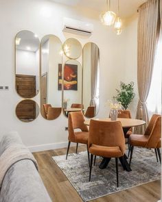 a dining room table with orange chairs and mirrors on the wall above it in front of a couch