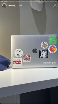 an apple laptop sitting on top of a white desk next to a blue hat and lamp