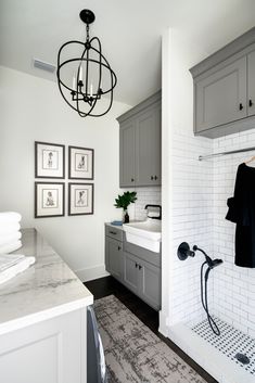 a bathroom with gray cabinets and white tile walls, a chandelier hanging from the ceiling