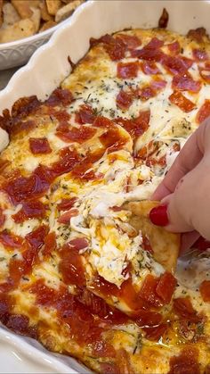 a person is taking a piece of pizza from a casserole dish with cheese and pepperoni