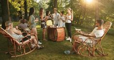 group of people sitting and standing around in the park talking to each other while having drinks