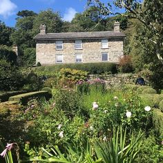 an old stone house surrounded by lush green plants and flowers on a sunny day with blue skies in the background