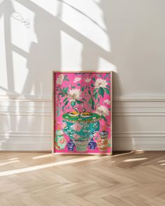 a pink and blue vase with white flowers on it in front of a wooden floor