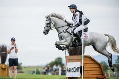 a man riding on the back of a white horse jumping over a wooden obstacle in an open field