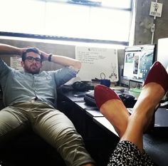 a man and woman sitting at a desk with their feet up