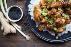 a black plate topped with chicken and rice next to sliced celery on top of a wooden table