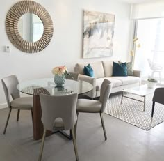 a living room filled with furniture and a round glass table surrounded by gray chairs next to a white couch