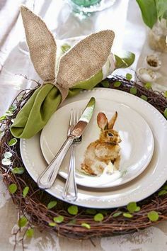 the table is set with plates, silverware and bunny rabbit napkins on it