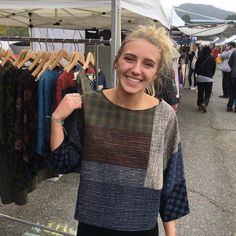 a woman standing in front of a rack of clothes at an outdoor market smiling for the camera