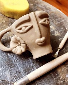 a clay mask sitting on top of a wooden table next to a pen and paper