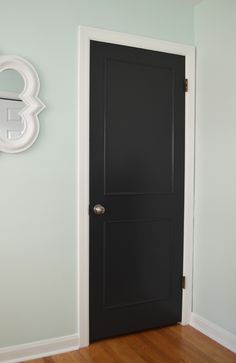 a black door is in the corner of a room with wood floors and white walls