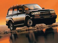 an suv is parked on the rocks by the water's edge with orange sky in the background