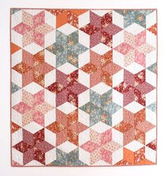 an orange and pink quilt is hanging on the wall