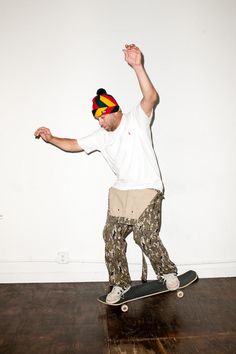 a man riding a skateboard on top of a hard wood floored floor next to a white wall