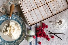 a table topped with plates and desserts covered in frosting next to raspberries