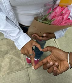 two people standing next to each other holding flowers and pointing fingers at the flower bouquet