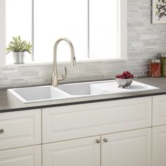 a white kitchen sink sitting under a window next to a vase with flowers on it