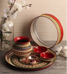 a red and gold plate with two cups on it next to a vase filled with flowers