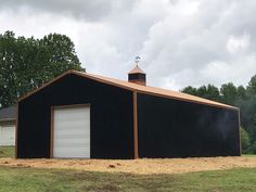 a large black barn sitting on top of a lush green field