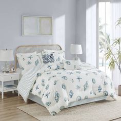 a bed with white and blue comforters on top of it in a room next to a window