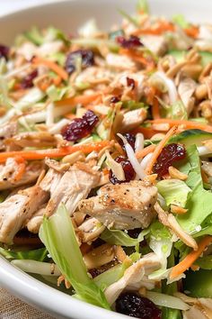 a salad with chicken, cranberries and lettuce in a white bowl