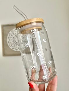 a person holding up a glass jar with hearts on it and a straw in the bottom