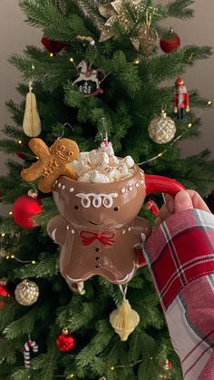 someone is holding up a mug in front of a christmas tree with ornaments on it