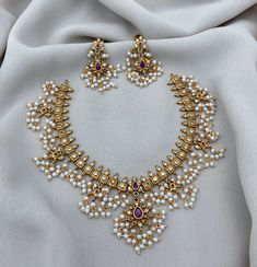 an elaborate necklace and earring set with pearls, rubs and stones on a white cloth