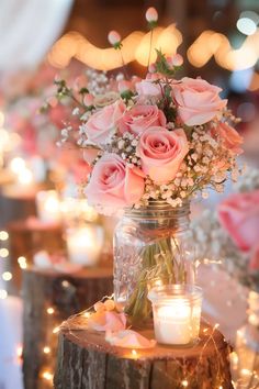 a vase filled with pink roses sitting on top of a wooden table next to candles