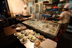 two chefs preparing food in a kitchen behind a counter with plates and bowls on it