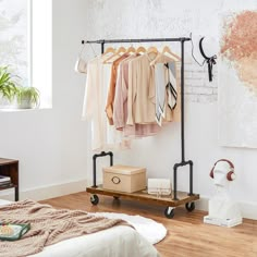 an iron rack with clothes hanging on it next to a bed in a white room