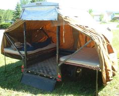 a tent that is in the grass with a man laying on it and another person sleeping inside