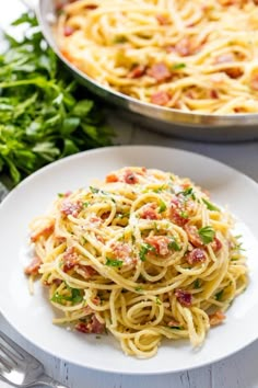 pasta with bacon and parsley on a white plate next to a skillet filled with sauce