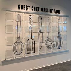 a display case with various kitchen utensils on the wall and in front of it is a sign that says guest chef wall of fame